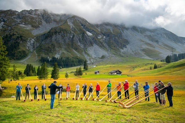 Les participants au cours de cor des Alpes s’entraînent en plein air. Le vaste paysage et les premières notes du cor des Alpes se fondent en une expérience inoubliable.