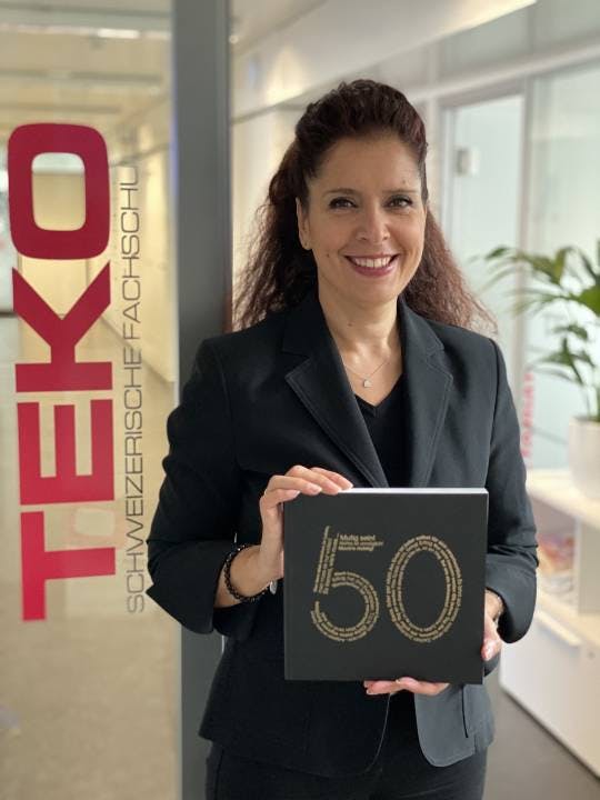Stolz präsentiert TEKO Basel Schulleiterin Terry Tschumi das Jubiläumsbuch mit 50 spannenden TEKO Erfolgsgeschichten