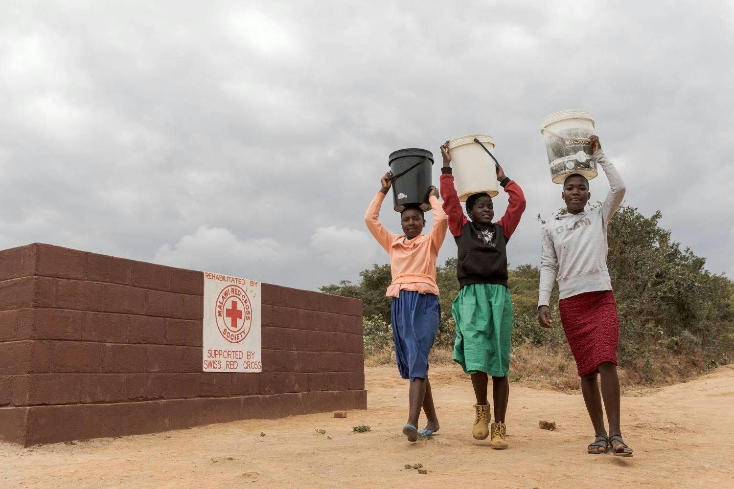 Des écolières malawites vont chercher de l’eau pour le jardin de l’école. Le point d’eau près de l’école a été remis en état par la Croix-Rouge suisse.